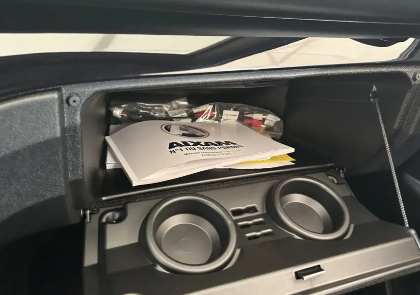 Vue intérieure du coffre à gants ouvert d'une Aixam Ambition 0.5 City Sport avec manuel et porte-gobelets visibles.