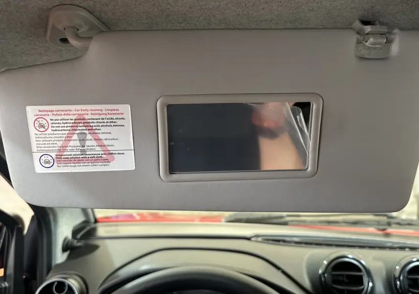 Vue intérieure centrée sur le pare-soleil avec miroir, tableau de bord et volant d'une Aixam Ambition rouge 2026.