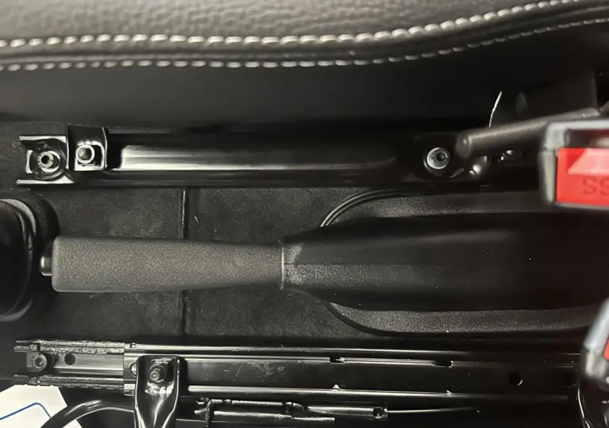 Vue rapprochée de la poignée de frein à main noire et du mécanisme sous le siège d’une Aixam Ambition 0.5 City Sport.