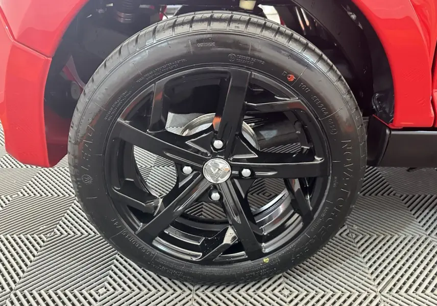 Gros plan sur la roue avant droite noire d’une Aixam Ambition 0.5 City Sport rouge, avec partie de la carrosserie visible.