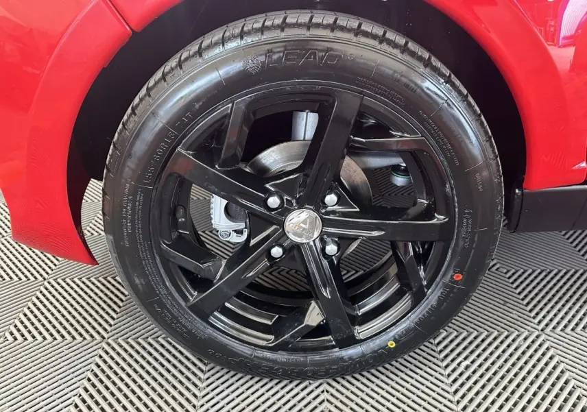 Gros plan sur la roue avant droite noire brillante d'une Aixam Ambition 0.5 City Sport rouge.