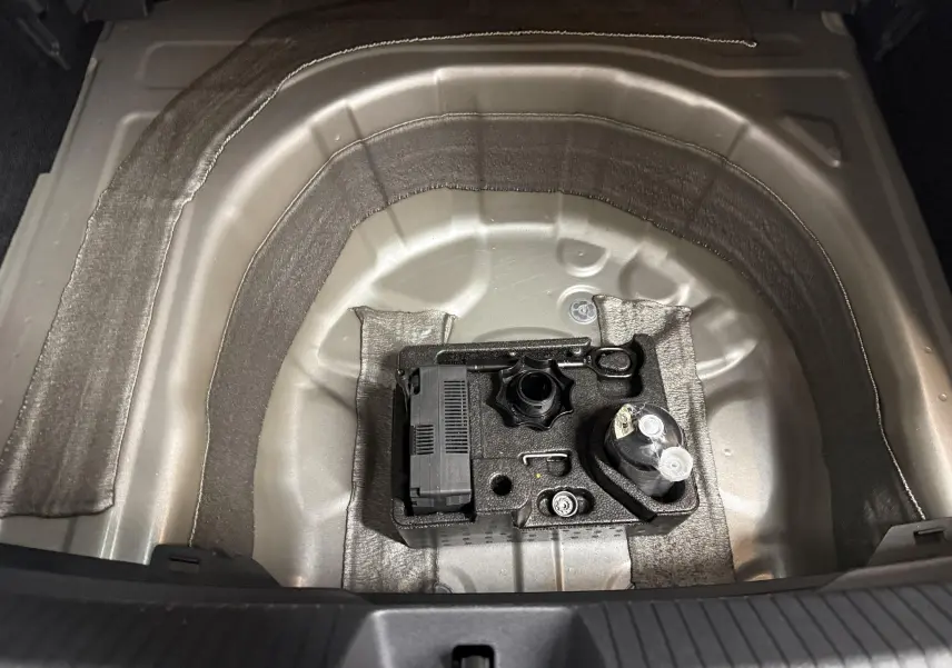 Coffre ouvert du Volkswagen Taigo 2025, vue plongeante sur la roue de secours et outils rangés dans un compartiment argent métallisé.