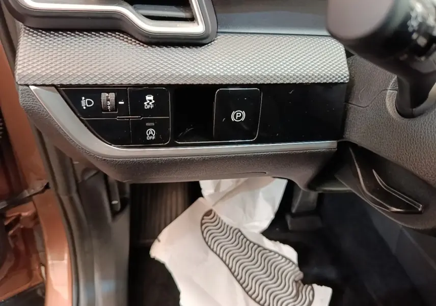 Détail intérieur côté gauche du tableau de bord beige du KIA SPORTAGE 2022 avec commandes d’éclairage et frein à main électrique.