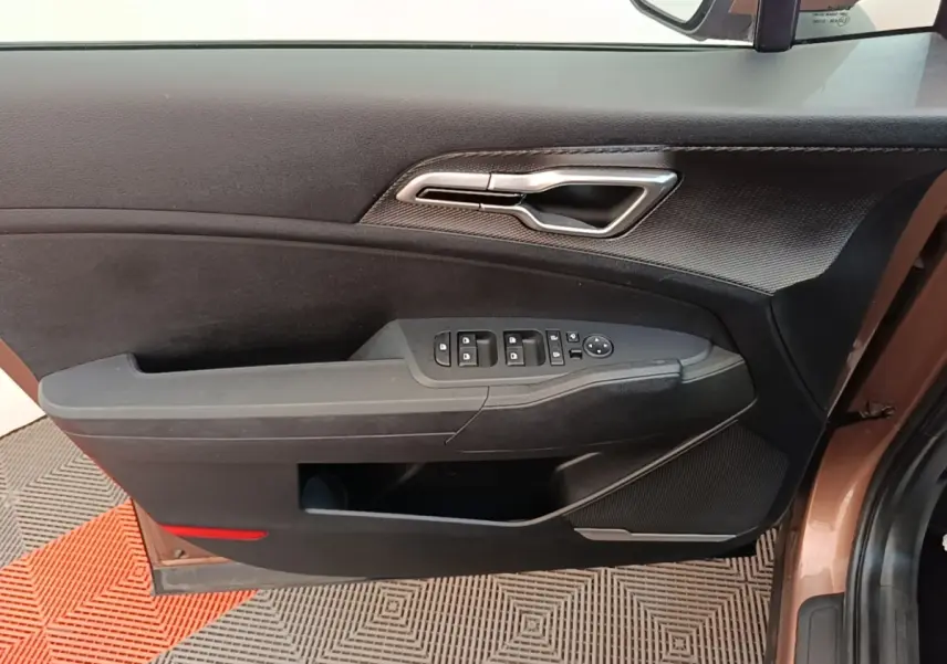 Intérieur côté gauche de la porte avant beige du KIA SPORTAGE 2022 avec commandes électriques et poignée argentée.