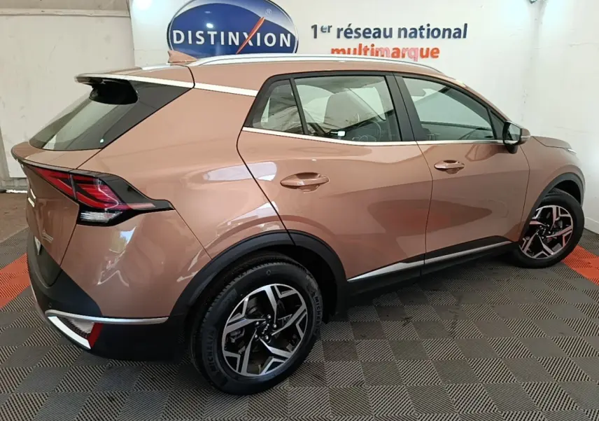 KIA Sportage beige vue 3/4 arrière droit, avec jantes alliage et feux arrière LED distinctifs.