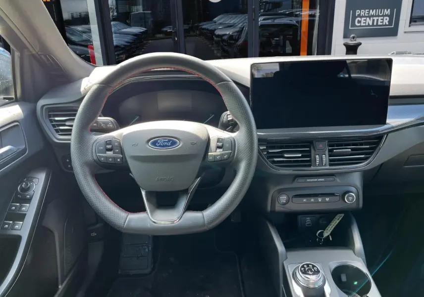 Vue intérieure du poste de conduite de la Ford Focus SW 2025, volant avec surpiqûres rouges et écran tactile central.