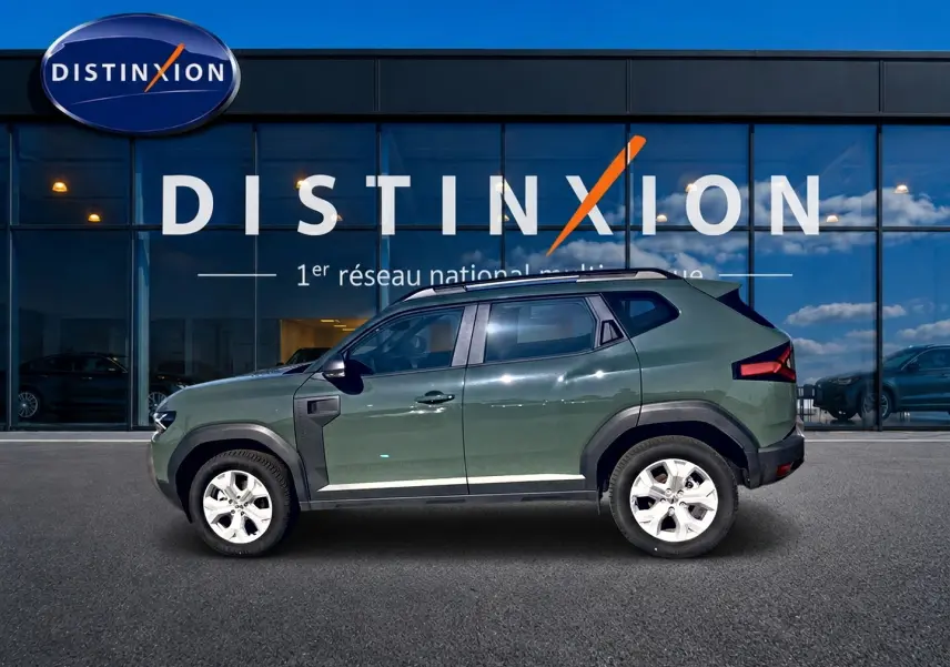 Profil droit du Dacia Duster 2026 kaki lichen avec barres de toit et jantes alu devant une vitrine Distinxion.