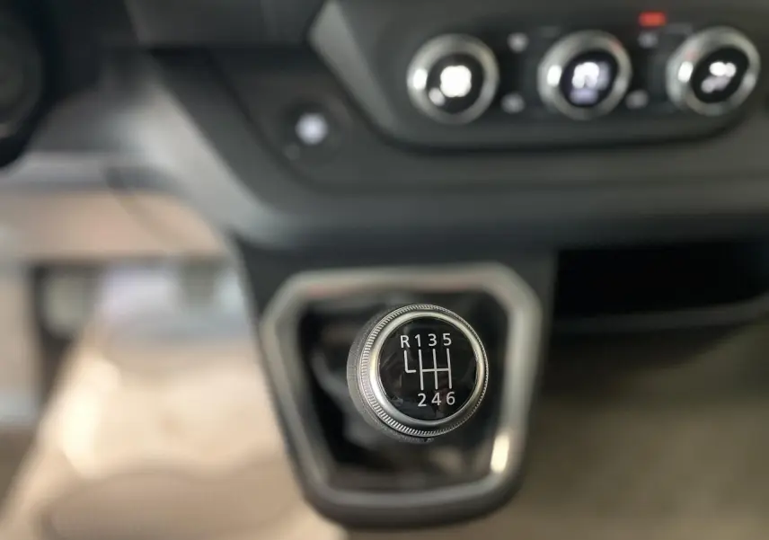 Gros plan sur le levier de vitesses manuel du Renault Trafic Fourgon, avec commandes de climatisation en arrière-plan.