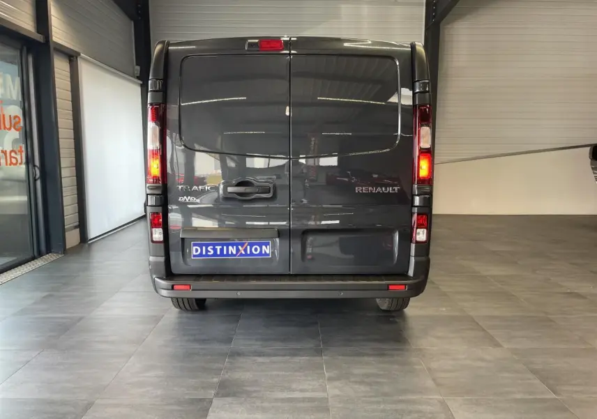Vue arrière du Renault Trafic Fourgon gris Comète avec feux allumés et plaque Distinxion visible en intérieur showroom.