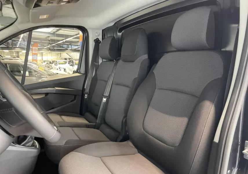Intérieur du Renault Trafic Fourgon gris Comète, vue côté conducteur montrant les sièges avant en tissu noir.