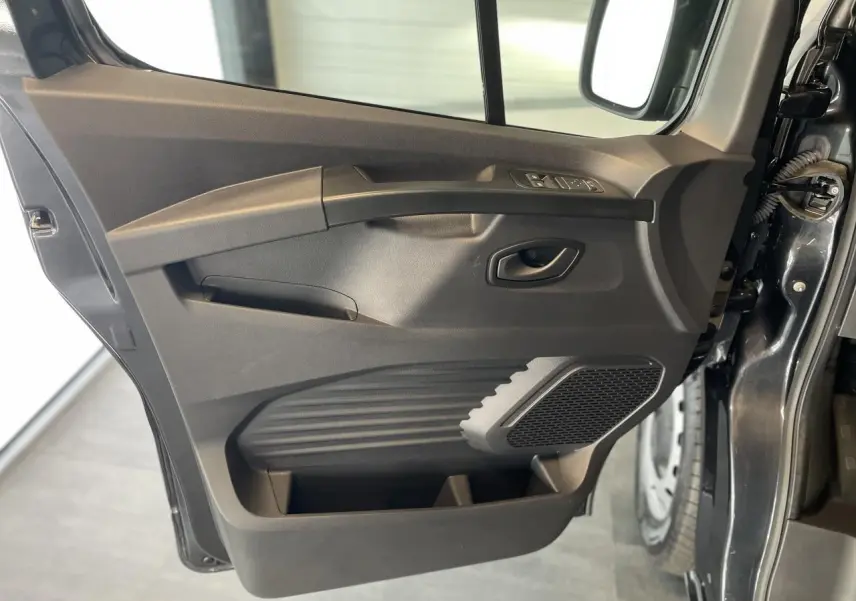 Vue rapprochée de la porte avant gauche gris comète du Renault Trafic Fourgon, avec commandes de vitres et haut-parleur intégré.