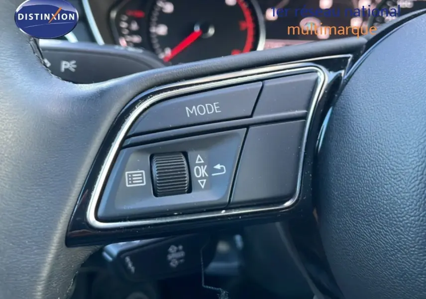 Gros plan sur les commandes gauche du volant noir de l'Audi A4 Avant gris Manhattan, avec tableau de bord flou en arrière-plan.