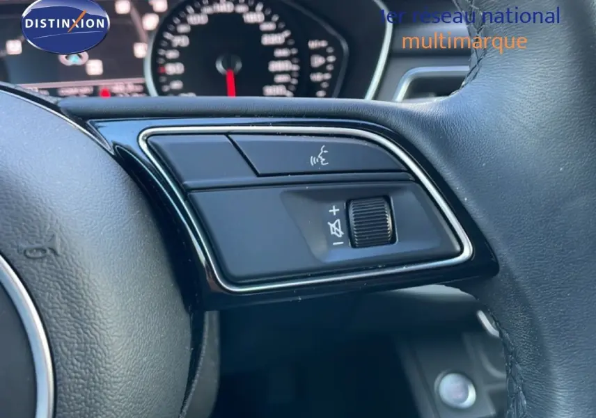 Gros plan sur les commandes vocales et volume au volant cuir d'une Audi A4 Avant gris Manhattan, tableau de bord flou en arrière-plan.