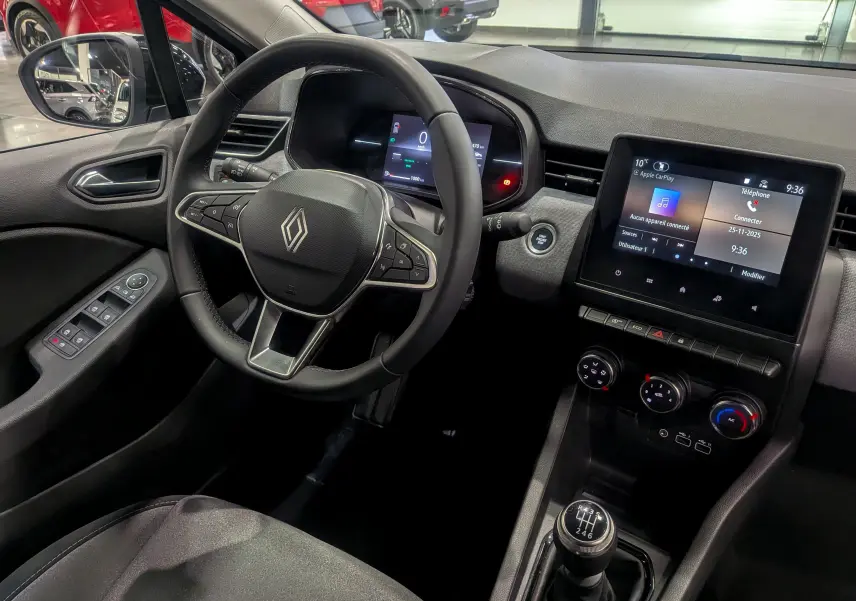 Vue intérieure côté conducteur de la Renault Clio V gris Rafale, avec volant multifonctions et écran tactile central.