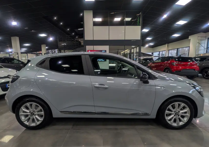 Profil côté gauche de la Renault Clio V 2025 gris Rafale en intérieur, soulignant ses jantes alliage et lignes épurées.