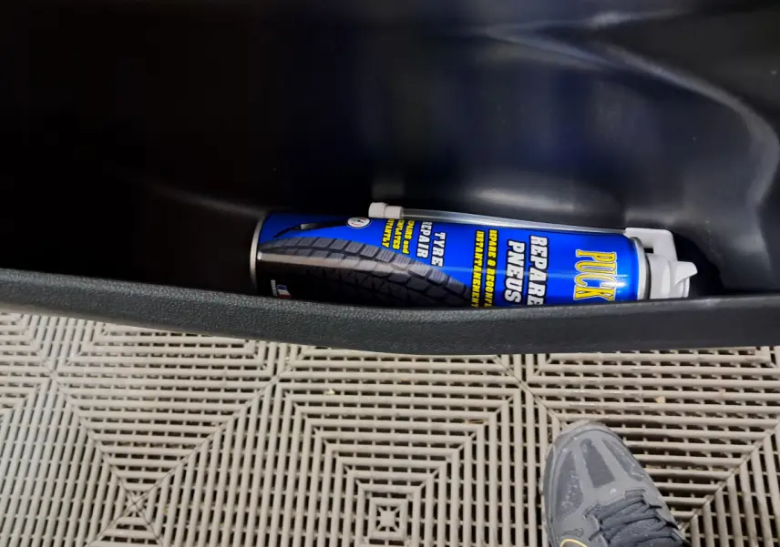 Vue intérieure du coffre latéral d'une Aixam Minauto E chic 2026 verte, avec bombe de réparation pneus visible.