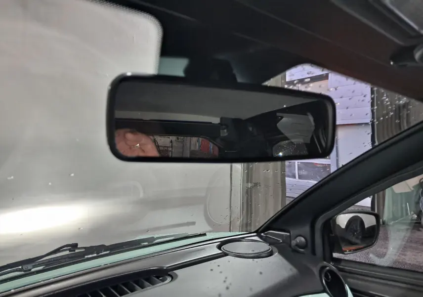 Vue intérieure centrée sur le rétroviseur intérieur d'une Aixam Minauto E chic 2026 vert, avec rétroviseur extérieur caméra côté conducteur visible.