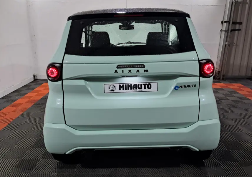 Vue arrière d'une AIXAM MINAUTO E chic 2026 vert clair avec feux ronds allumés et logo eMINAUTO visible à droite.