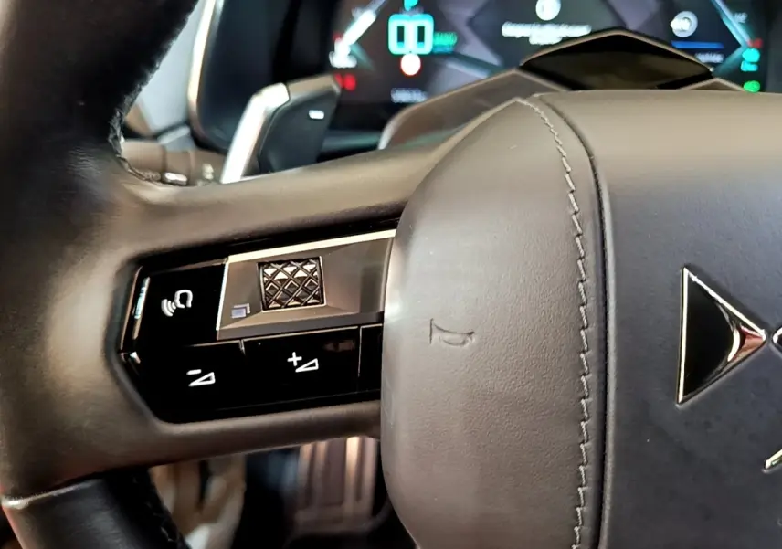 Gros plan sur le volant cuir noir du DS7 Crossback E-TENSE 4x4 300 avec commandes multifonctions et logo DS visible.