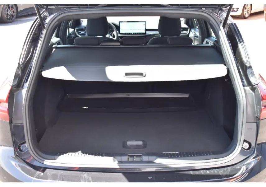 Vue arrière du coffre ouvert d'une Ford Focus SW 2025 Agate Black Metallic, avec cache-bagages déployé et intérieur noir.