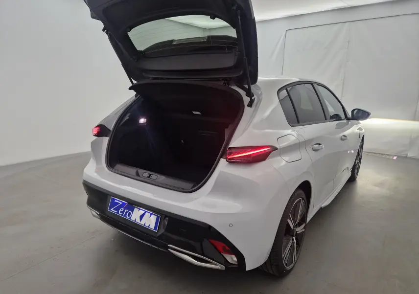 Vue 3/4 arrière droite d'une Peugeot 308 blanche Okenite avec coffre ouvert et feux arrière allumés dans un studio.