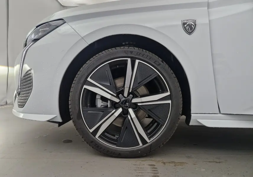 Gros plan sur la roue avant gauche d'une Peugeot 308 blanche Okenite avec jante alliage et logo GT visible sur l'aile.