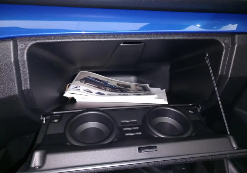 Intérieur de la boîte à gants ouverte d'une Aixam Mega bleu, avec porte-gobelets et documentation visible.