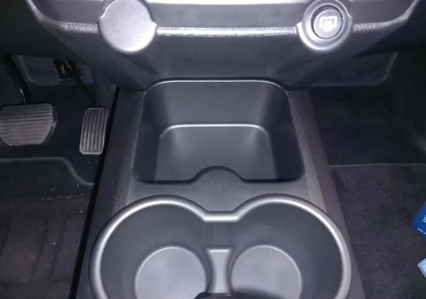 Gros plan intérieur sur la console centrale noire avec porte-gobelets et pédales au sol du côté conducteur.