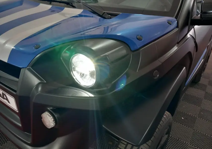 Gros plan avant droit sur l'AIXAM MEGA bleu électrique avec phare allumé et rétroviseur caméra côté conducteur.