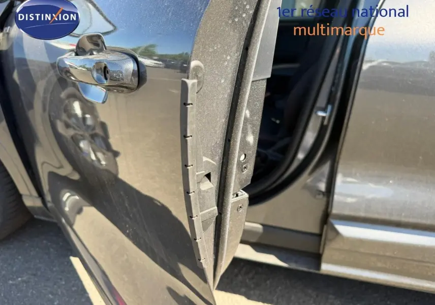 Vue rapprochée de la porte avant gauche ouverte d’un Ford Kuga 2024 gris magnétique métal, avec reflet et poignée chromée.