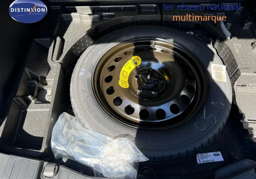 Roue de secours noire dans le coffre d’un Ford Kuga 2024 gris magnétique, avec kit de réparation plastique à côté.