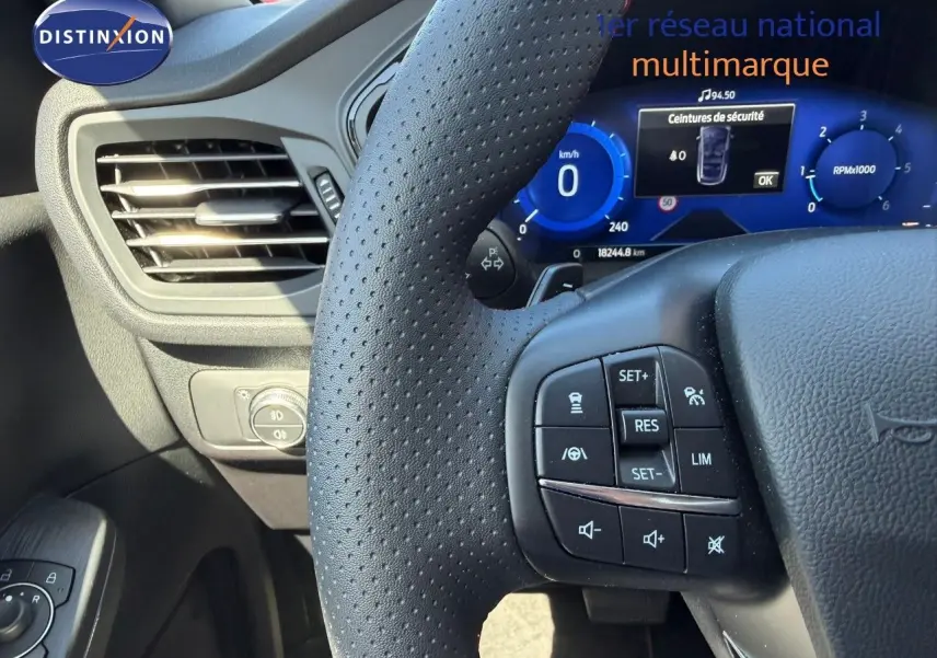 Vue rapprochée du volant perforé et du tableau de bord numérique bleu d’un Ford Kuga 2024 gris magnétique.