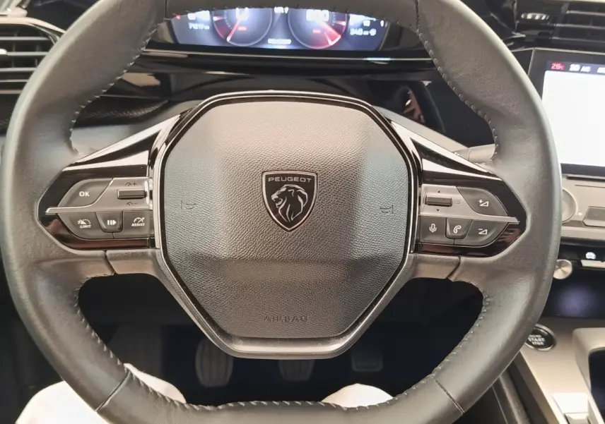 Vue rapprochée du volant cuir noir de la Peugeot 308 2023 avec commandes multifonctions et tableau de bord digital.