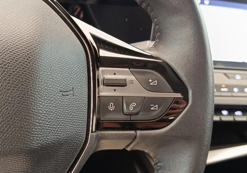 Gros plan sur les commandes du volant en cuir noir de la Peugeot 308 blanche, version PureTech 130 S&S ACTIVE PACK 2023.