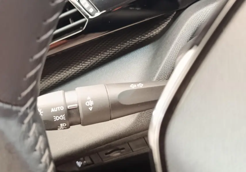 Gros plan sur la commande des clignotants et feux à gauche du volant cuir dans l’habitacle d’une Peugeot 308 blanche.