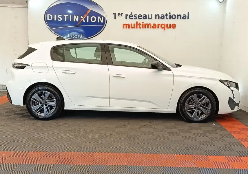 Profil droit d'une Peugeot 308 blanche 2023 avec jantes alliage et feux LED, en intérieur showroom.