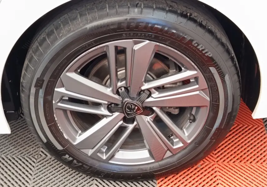 Gros plan sur la roue avant droite d'une Peugeot 308 blanche, avec jante alliage au design moderne.