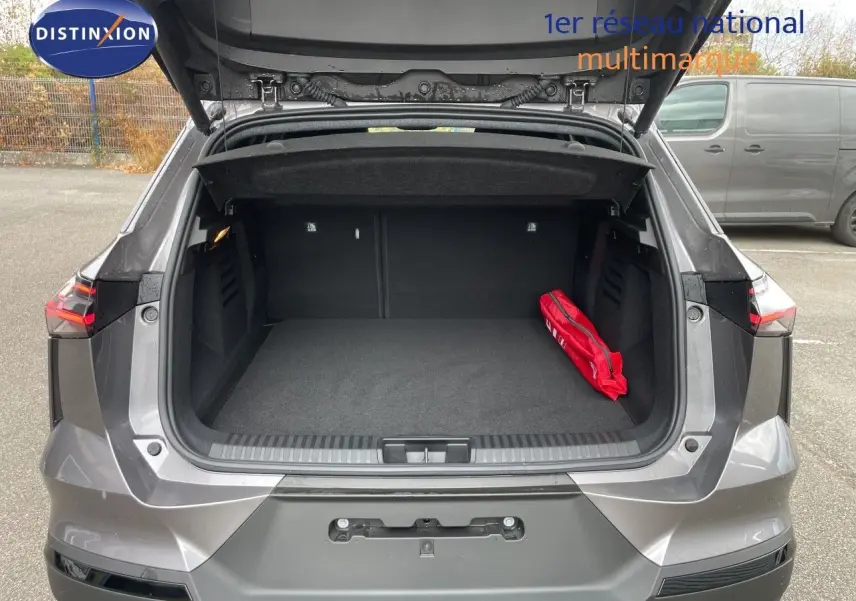Coffre ouvert vu de l'arrière d'une Renault Symbioz gris Cassiopée métal, avec un kit de sécurité rouge à droite.