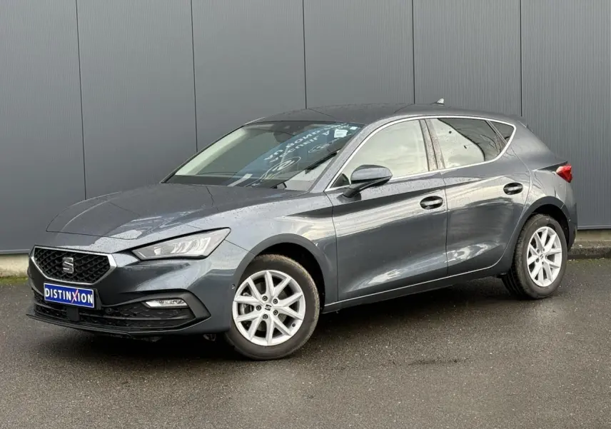 SEAT Leon 1.5 TSI 115 Style gris magnétique en 3/4 avant droit, jantes alliage 16 pouces visibles, stationnée sur sol humide.