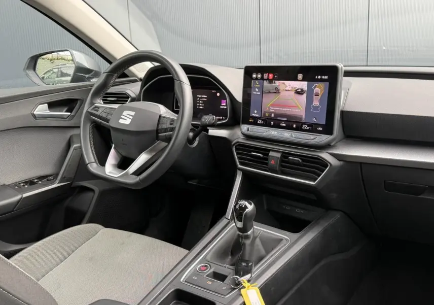 Vue intérieure côté conducteur du SEAT Leon 1.5 TSI gris, avec volant cuir multifonction et écran tactile affichant la caméra de recul.