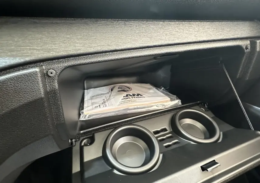 Vue intérieure du coffre à gants ouvert de l'AIXAM AMBITION blanc 2026, avec porte-gobelets et manuel visible.