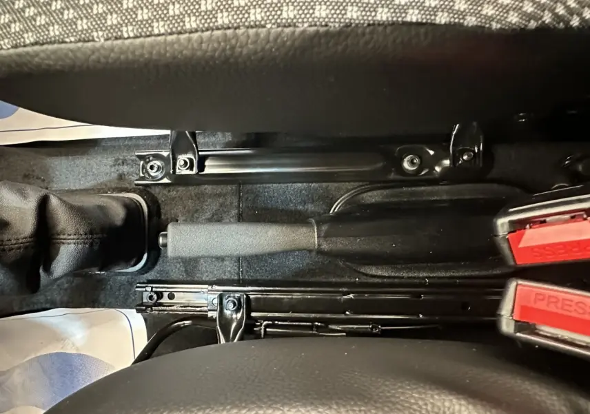 Vue rapprochée de la poignée de frein à main et des ceintures de sécurité rouges entre les sièges noirs d’une Aixam Ambition blanche.