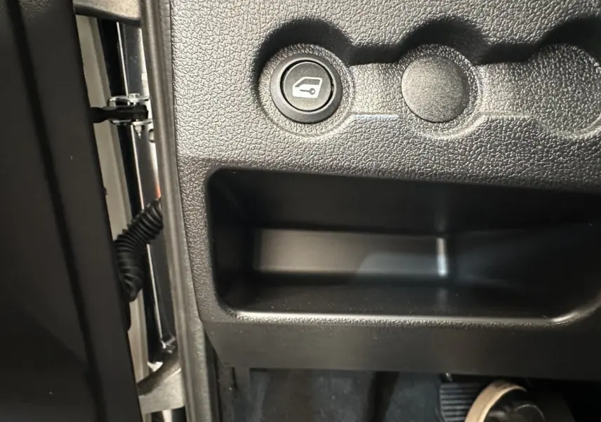 Détail intérieur montrant le bouton d'ouverture du coffre sur le tableau de bord noir de l'AIXAM Ambition 0.5 City Pack.