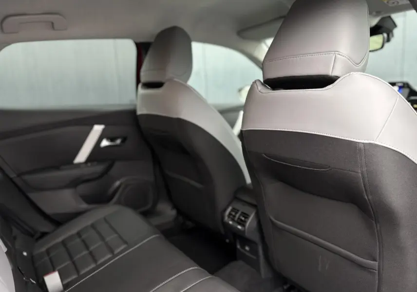 Vue intérieure arrière côté gauche de la Citroën C4 Hybrid 2025, sièges bicolores gris clair et noir avec surpiqûres blanches.