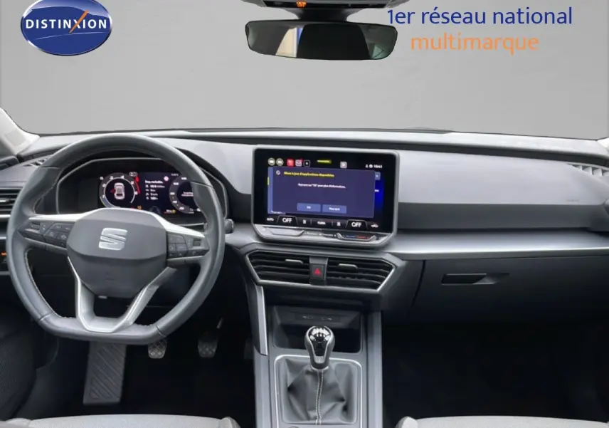 Vue intérieure avant du tableau de bord gris noir du SEAT LEON 2025 avec volant cuir multifonction et écran tactile central.