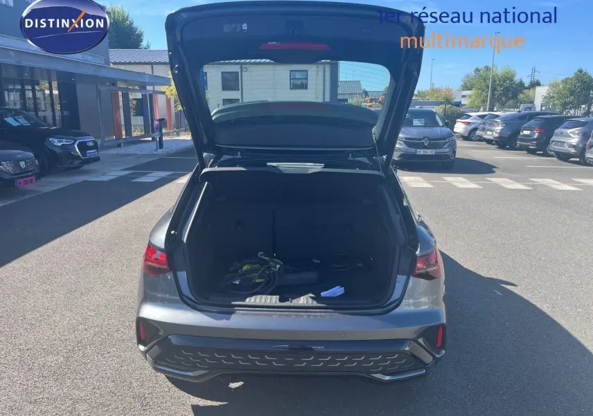 Vue arrière avec coffre ouvert d'une Audi A3 Sportback 40 TFSIe gris Daytona Metal, montrant le volume de chargement et câbles de recharge.