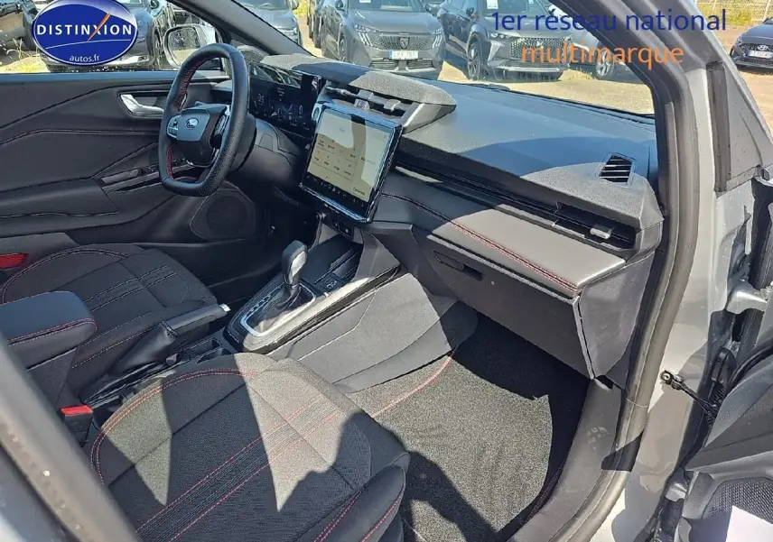 Intérieur avant droit du Ford Puma gris cactus 2025, avec sièges tissu noir et surpiqûres rouges, écran tactile central visible.