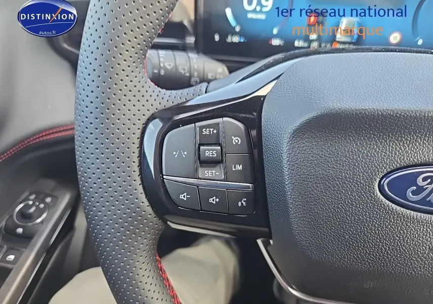 Gros plan sur le volant perforé avec surpiqûres rouges du Ford Puma 2025, boutons de régulateur de vitesse visibles.