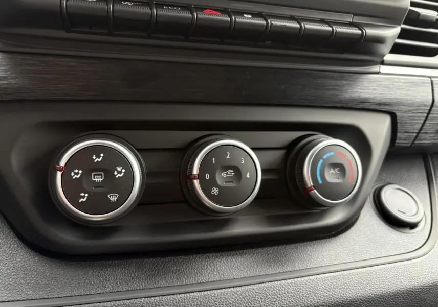 Gros plan sur les commandes de climatisation du tableau de bord noir du Renault Trafic Fourgon Gris Urbain 2025.