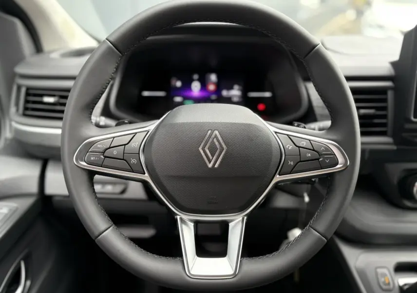 Vue rapprochée du volant en cuir multifonction du Renault Trafic Fourgon 2025, avec commandes intégrées et tableau de bord numérique flou.
